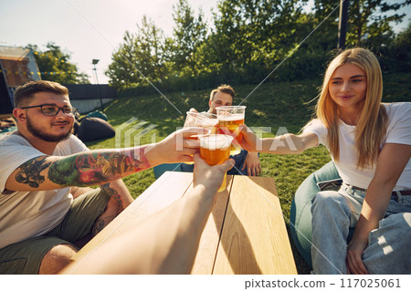 Happy young smiling people sitting outdoors in cafe, restaurant, enjoying refreshing beer, clinking glasses. Celebration, party Happy young smiling people sitting outdoors in cafe, restaurant, enjoying refreshing beer, clinking glasses. Celebration, party 117025061