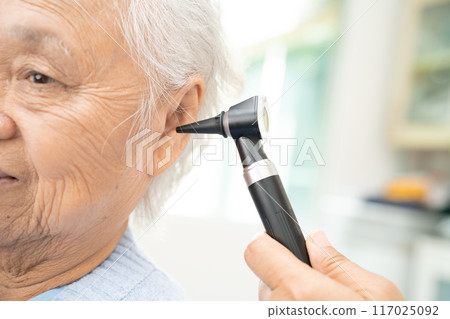 Audiologist or ENT doctor use otoscope checking ear of asian senior woman patient treating hearing loss problem. 117025092