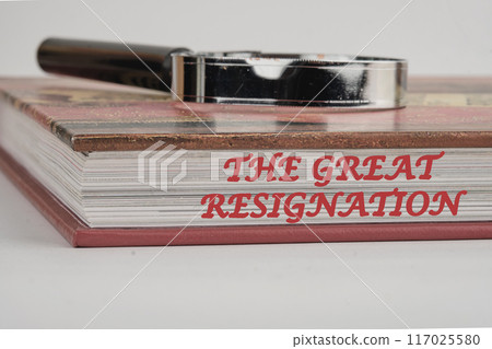Text THE GREAT RESIGNATION, mass voluntary exodus from the workforce. THE GREAT RESIGNATION on the end of the book with a magnifying glass on top on a white background Text THE GREAT RESIGNATION, mass voluntary exodus from the workforce. THE GREAT RESIGNATION on the end of the book with a magnifying glass on top on a white background 117025580