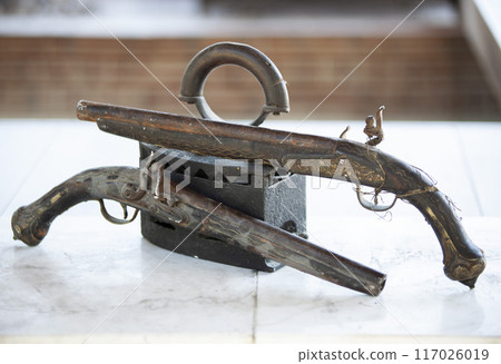 Antique charcoal iron and antique patterned revolvers with forged grips. Antique metalware. Horizontal 117026019