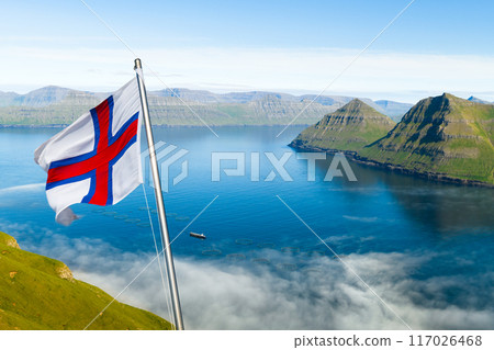National Faroese flag waving against a background of foggy fjord National Faroese flag waving against a background of foggy fjord 117026468