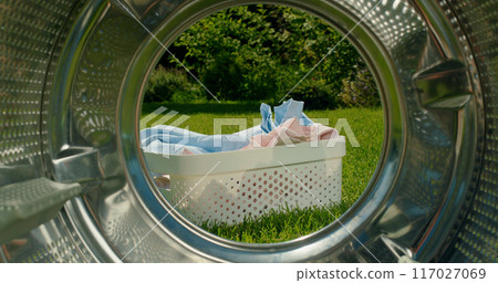 Laundry basket with clothes on green grass, viewed from inside a washing machine drum. 117027069