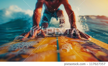 Surfer riding the waves on a sunny day, close-up of hands on the surfboard, enjoying the thrill and adventure of surfing. 117027357