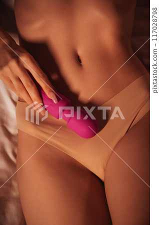 pink vibrator in female hand on stomach of woman girl with a sexy body in panties lying on bed. Sex toys for female satisfaction and orgasm pink vibrator in female hand on stomach of woman girl with a sexy body in panties lying on bed. Sex toys for female satisfaction and orgasm 117028798