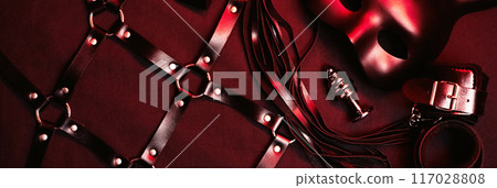 set of BDSM sex toys with handcuffs, whip flogger, butt anal plug for submission and domination on red background 117028808