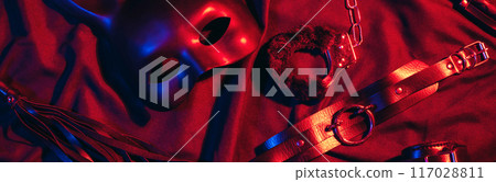 set of BDSM sex toys with handcuffs, a whip flogger and a mask for submission and domination on a red background 117028811
