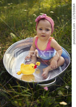 baby in a metal tub plays with rubber ducklings in the summer garden 117030064