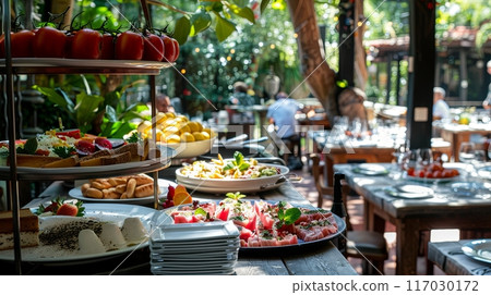 brunch setting with various fresh dishes displayed on a table in a sunlit, outdoor restaurant 117030172