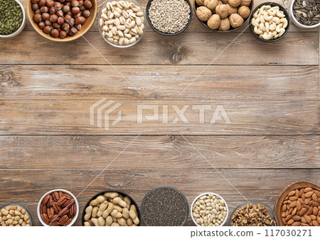 Mixed assorted nuts and seeds in various bowls on wooden table and space for text in the middle. 117030271