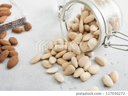 Glass jar with healthy raw almond whole and peeled nuts on white kitchen table. Glass jar with healthy raw almond whole and peeled nuts on white kitchen table. 117030272