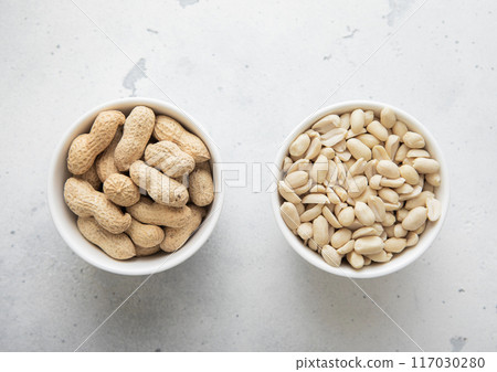 Bowls with whole and peeled healthy peanut nuts on light background. Bowls with whole and peeled healthy peanut nuts on light background. 117030280