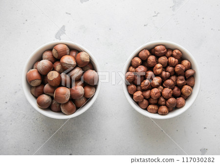 Bowls with whole and peeled healthy hazelnut nuts on light background. Bowls with whole and peeled healthy hazelnut nuts on light background. 117030282