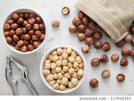 Whole and peeled hazelnut nuts with cracker and linen bag on light background Whole and peeled hazelnut nuts with cracker and linen bag on light background 117030283
