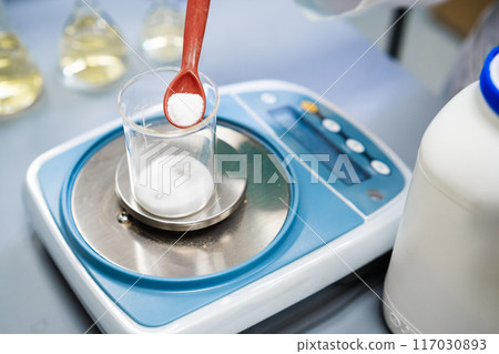 Using laboratory balances, a researcher weighs powder samples 117030893