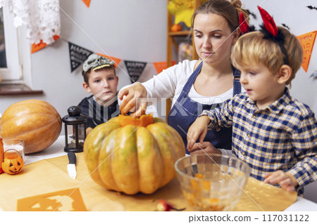 Family carving pumpkins at Halloween table Family carving pumpkins at Halloween table 117031122