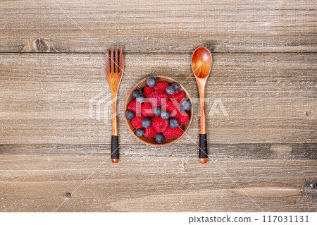 Mix of blueberries and raspberries in a plate with wooden fork and spoon. 117031131