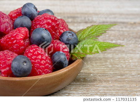 Plate with raspberries and blueberries with leaves on the wooden rustic table. 117031135