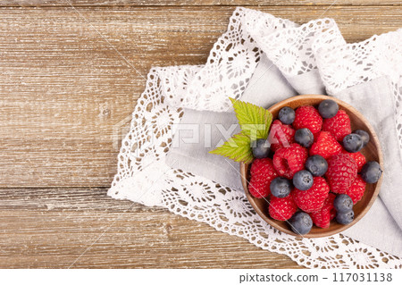 Plate with raspberries and blueberries on the wooden table with laced cloth. 117031138
