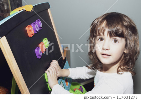 Toddler girl learning letters on the magnetic easel at home. 117031273