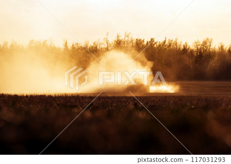 Tractor with a seeder is working in the dust in golden sunset light. 117031293