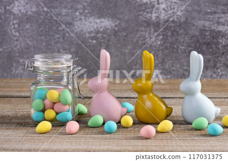 Easter composition with three bunnies and a jar with colorful candies. 117031375