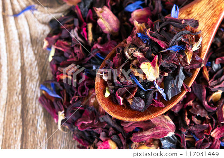 Tea mix of karkade, flowers and berries in a spoon and on the table. Tea mix of karkade, flowers and berries in a spoon and on the table. 117031449