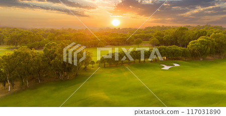Panorama of golf course at sunset with dramatic sky. Scenic panoramic view of golf fairway with pond. Golf field with beautiful pines 117031890