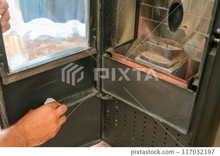 Close-up of a man cleaning the soot produced by the pellet stove in his living room, sustainable heat. Renewable energy. Close-up of a man cleaning the soot produced by the pellet stove in his living room, sustainable heat. Renewable energy. 117032197