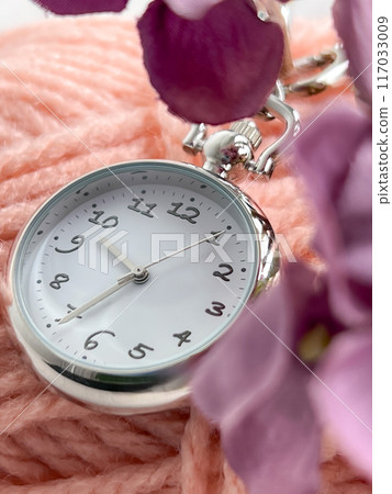 A silver pocket watch surrounded by pink threads and purple flowers, close-up shot creates an elegant atmosphere 117033009