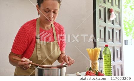 Housewife woman chef in kitchen apron cooking, preparing Italian meal in the home kitchen Housewife woman chef in kitchen apron cooking, preparing Italian meal in the home kitchen 117033269
