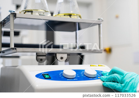 Chemist in rubber gloves places samples on the laboratory shaker in the lab Chemist in rubber gloves places samples on the laboratory shaker in the lab 117033526