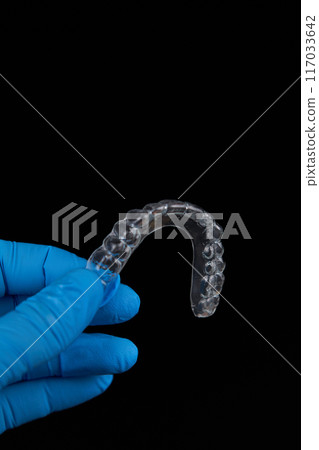 A person dressed in blue gloves holds a transparent mouthpiece 117033642