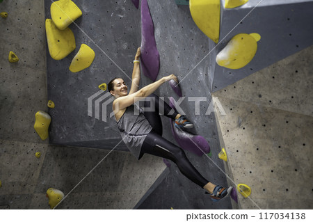 Happy fit woman climbing artificial boulder in 117034138