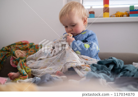 funny european kid playing with laundry basket on bed in cozy bedroom  117034870