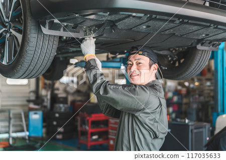 一名男性汽車修理工拆除底蓋，在升降機上的車輛下方進行維護、檢查和工作。 117035633