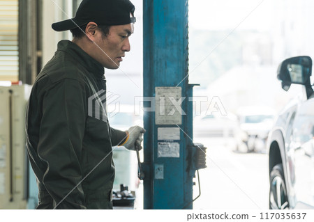 A male mechanic operating a lift at a maintenance workshop A male mechanic operating a lift at a maintenance workshop 117035637