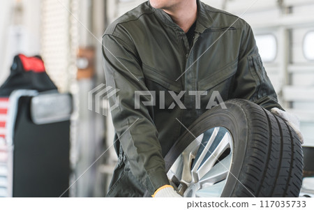 Male mechanic carrying tires at an auto repair shop (physical labor, heavy work, heavy, back pain) Male mechanic carrying tires at an auto repair shop (physical labor, heavy work, heavy, back pain) 117035733