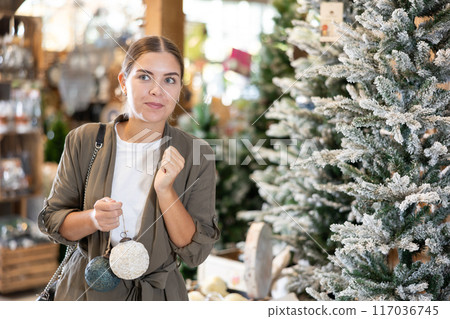 Girl buyer considers New Year and Christmas decorations ornaments for Christmas tree Girl buyer considers New Year and Christmas decorations ornaments for Christmas tree 117036745