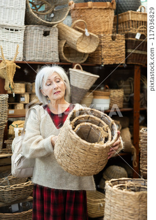 Senior woman looks at wicker basket in store. 117036829