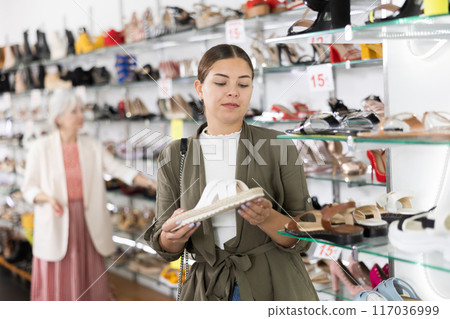 Young woman chooses fashionable summer shoes in shoe store Young woman chooses fashionable summer shoes in shoe store 117036999