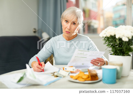 Focused aged woman making list of expenses at home table 117037160