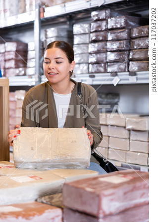 Female customer chooses briquettes with white clay in specialized store 117037202