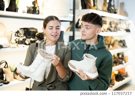 Young couple discussing choice of winter womens boots in shoe store 117037257