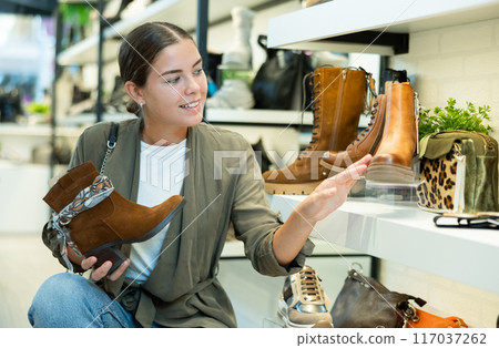 Girl buyer looks at footwear from new collection and picks up new pair of boots for winter. 117037262
