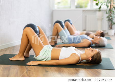 Family grandmother, mother and granddaughter perform fitness exercises lying on floor with softball. Family grandmother, mother and granddaughter perform fitness exercises lying on floor with softball. 117037286