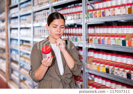 Woman buys jars of paint and glaze to coat pottery at a ceramic specialty store 117037311