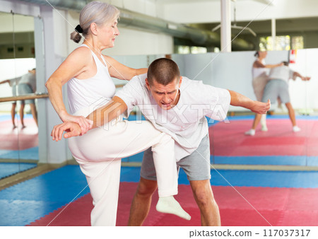 Mature woman performing knee strike during self-defence training 117037317