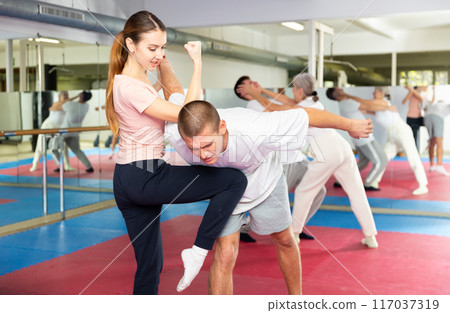 Girl with male opponent practicing elbow and knee strikes while locking arm 117037319