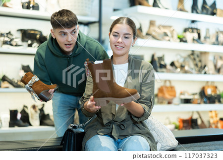 Guy male friend strongly recommends his young woman colleague to pay attention to model of boots 117037323