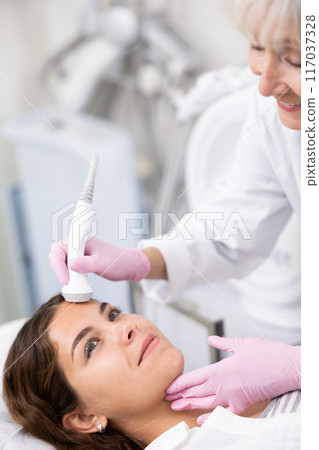 Young woman having face laser therapy procedure by specialist 117037328